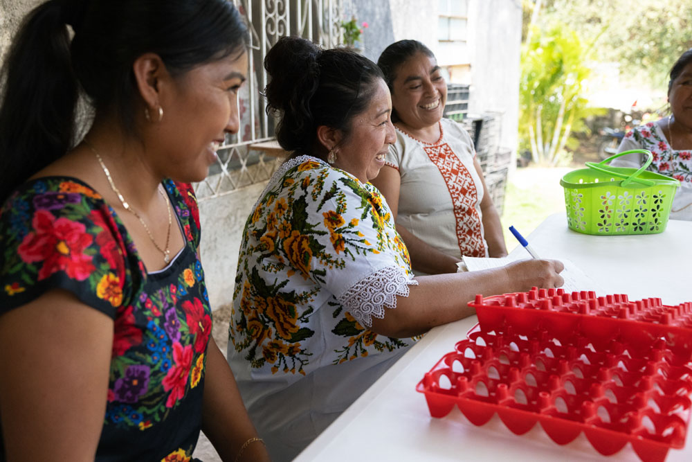 Three Mexican women sit at a table with an empty egg crate in front of them.