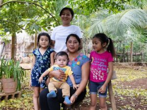 Two women and three children pose under a green tree.