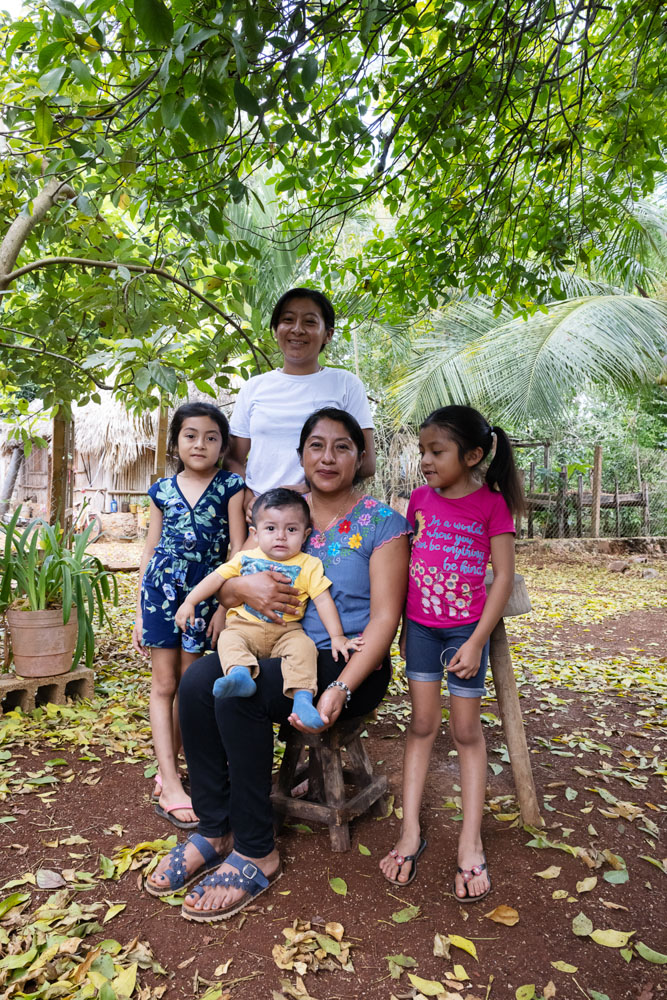 Two women and three children pose under a green tree.