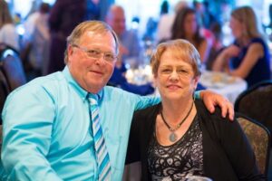 A man in a light blue shirt with his arm around a woman at a crowded event.
