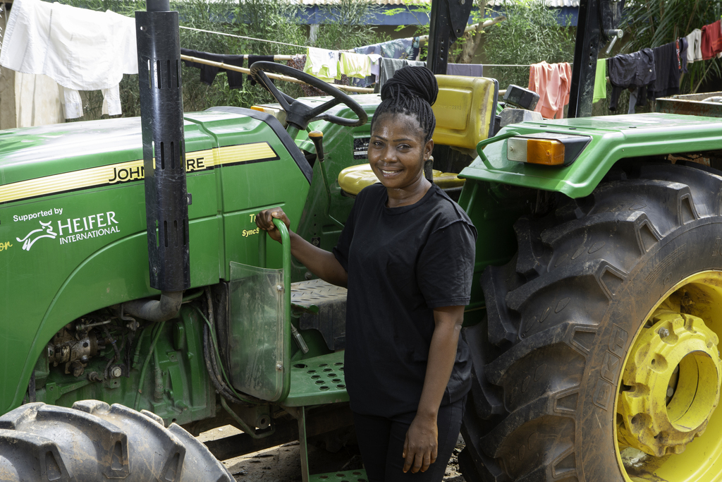 A woman farmer stands beside a tractor.