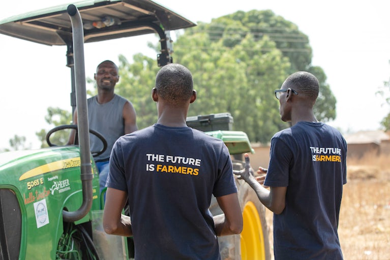 Two Heifer International project staff speaking to a man driving a tractor in Nigeria.