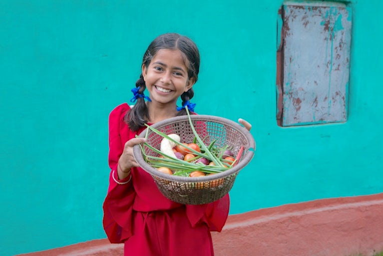 A child holding a basket full of vegetables.