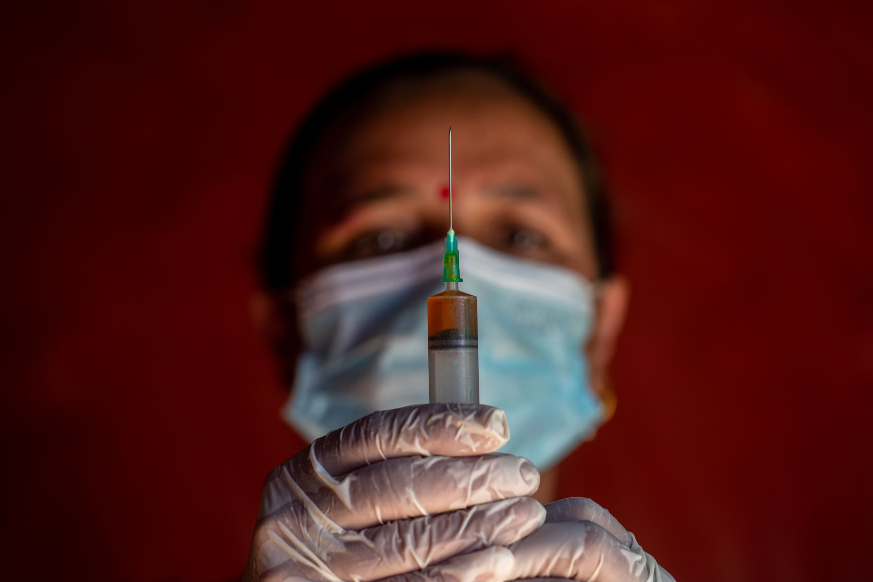 A woman wearing a mask and gloves holds a syringe.