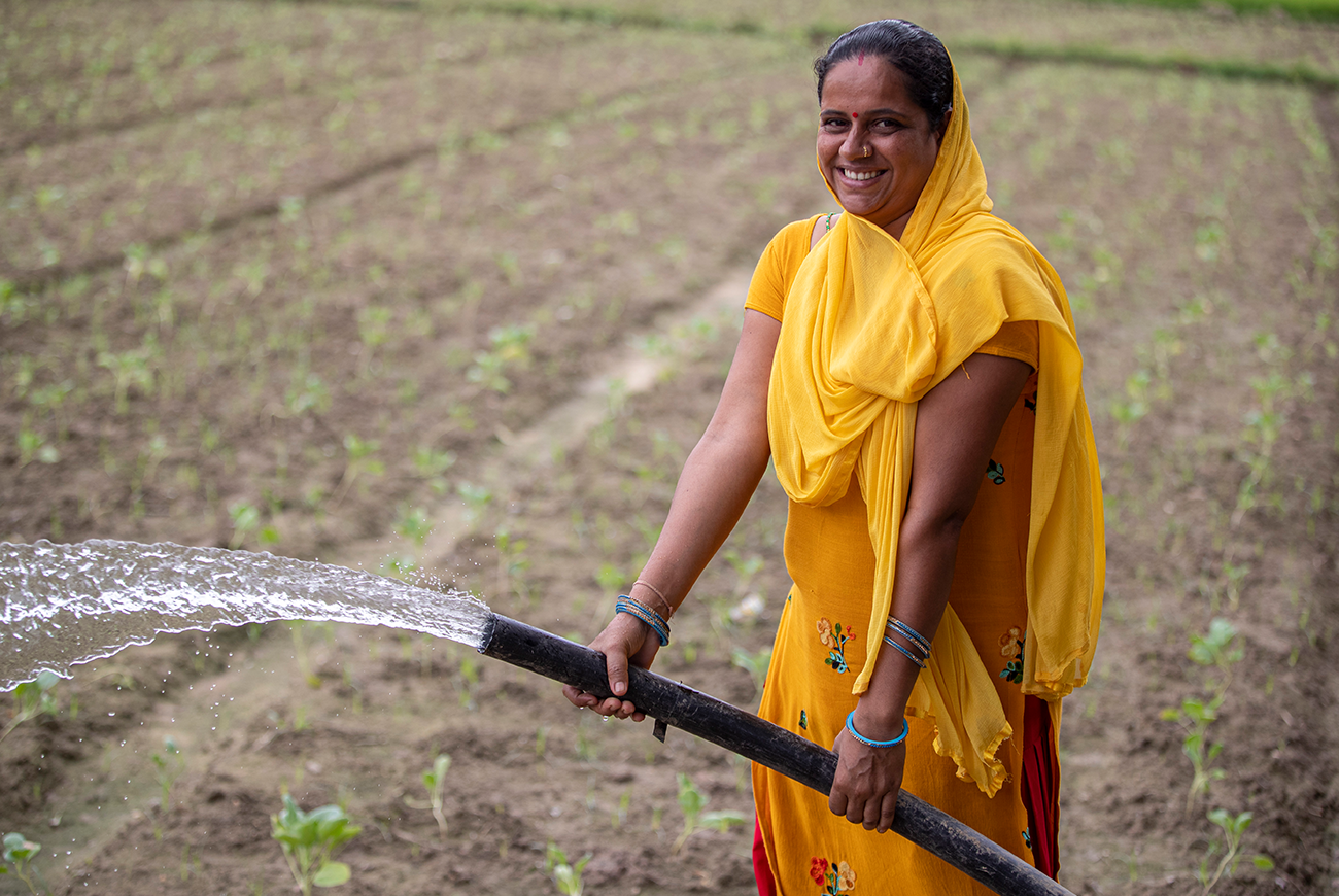 A woman sprays water from a hose on a field of vegetables.