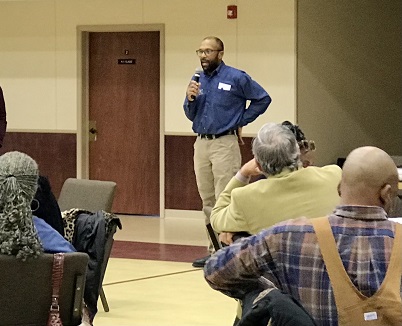 A speaker in a blue shirt engages with a group of attendees at an indoor event.