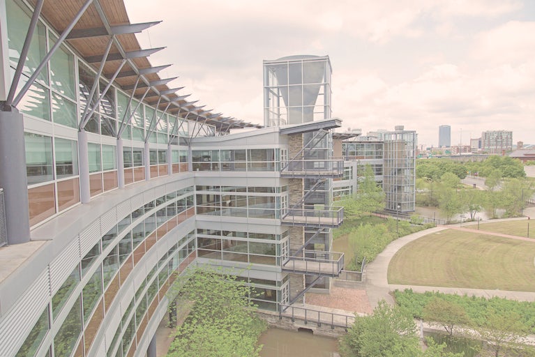 Heifer Headquarters, a glass and steel building, curves around wetlands and a manicured lawn with buildings in the downtown Little Rock area in the distance.
