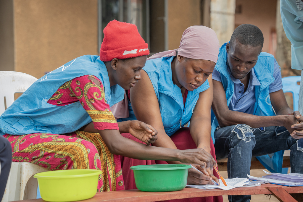 Women in a blue vests lean over papers.