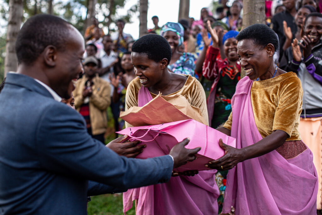Two women receive a wrapped gift as a crowd looks on.