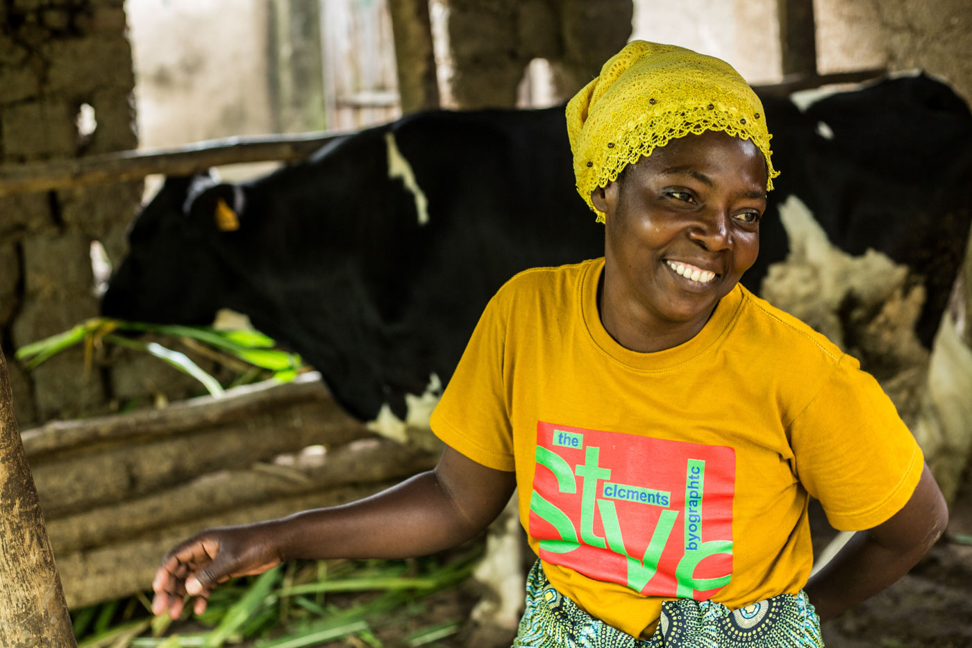 A woman dairy farmer in Rwanda smiling in front of her cow shed.