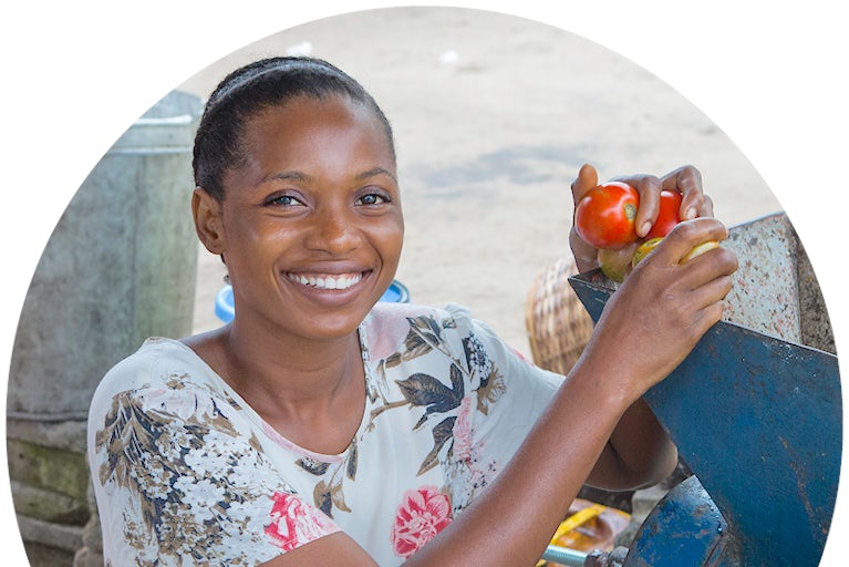 Smiling woman holds tomatoes near a processing machine.