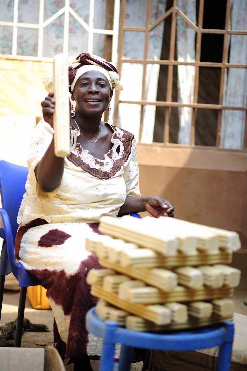 A sitting Ghanese woman proudly holds up a bar of soap she made for her growing business.