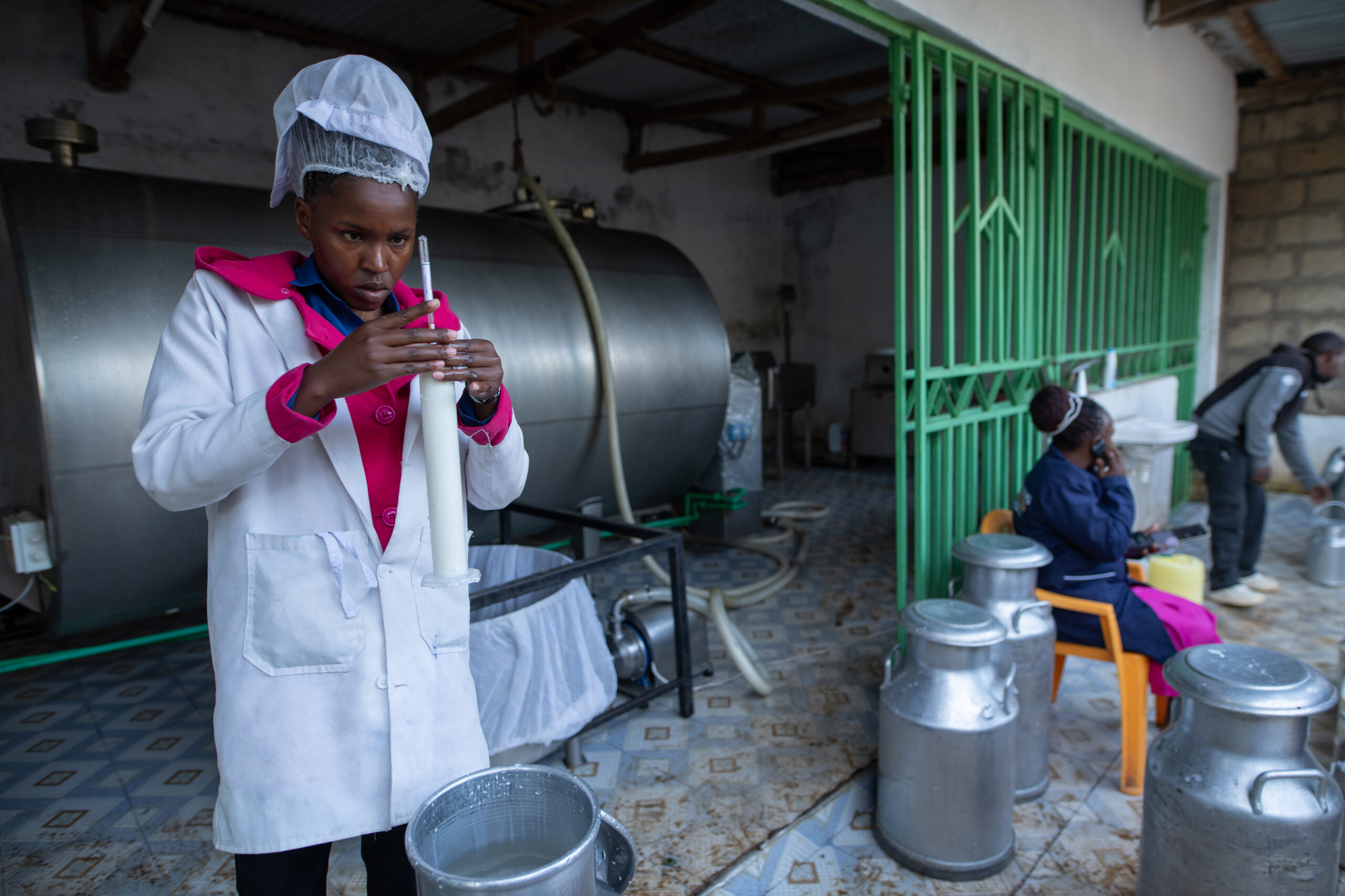 Woman in a lab coat measures milk inside a small dairy facility.