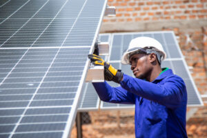A technician wearing a safety helmet maintains solar panels.