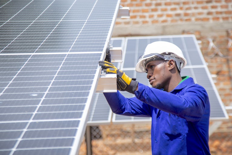 Worker in blue uniform and white hard hat installing solar panel on brick building. RetryClaude can make mistakes. Please double-check responses.