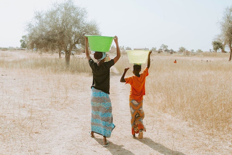 A woman and a child carrying water jugs atop their heads.