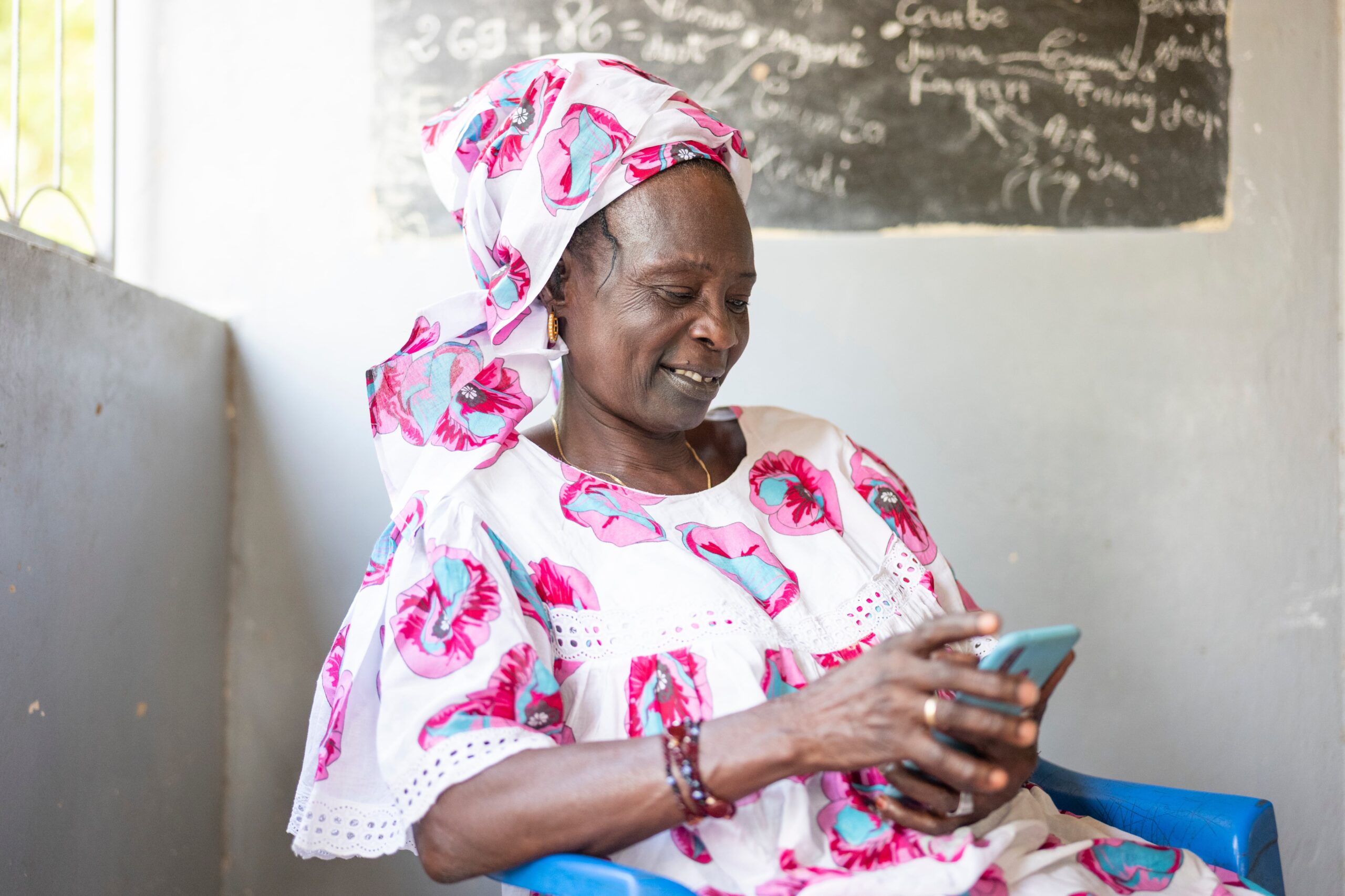 A Senegalese women sits on a chair and looks at her mobile phone.