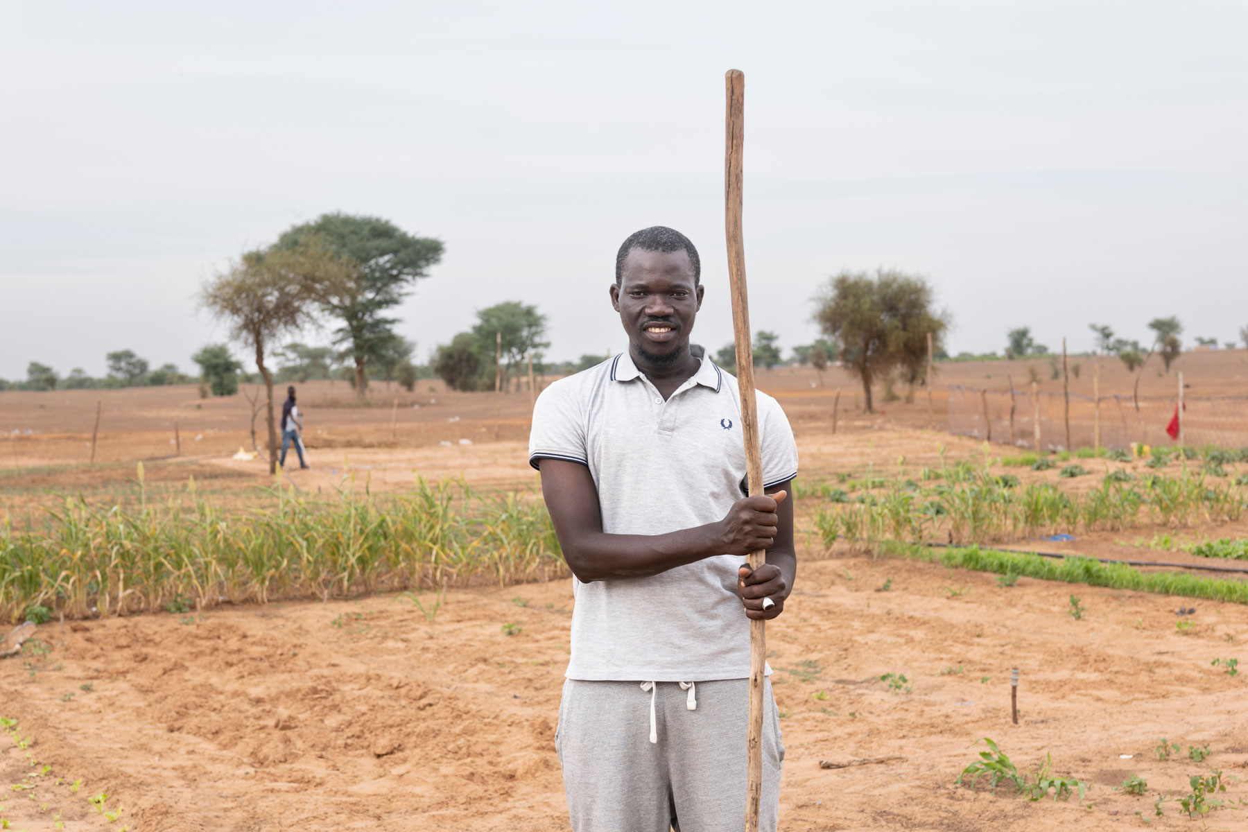 A Senegalese farmer holds a stick in a cultivated field.