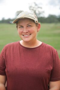 A woman wearing a baseball cap smiles at the camera.