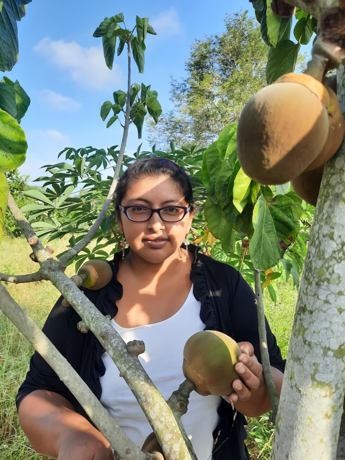 A woman stands next to a fruit tree in Ecuador.