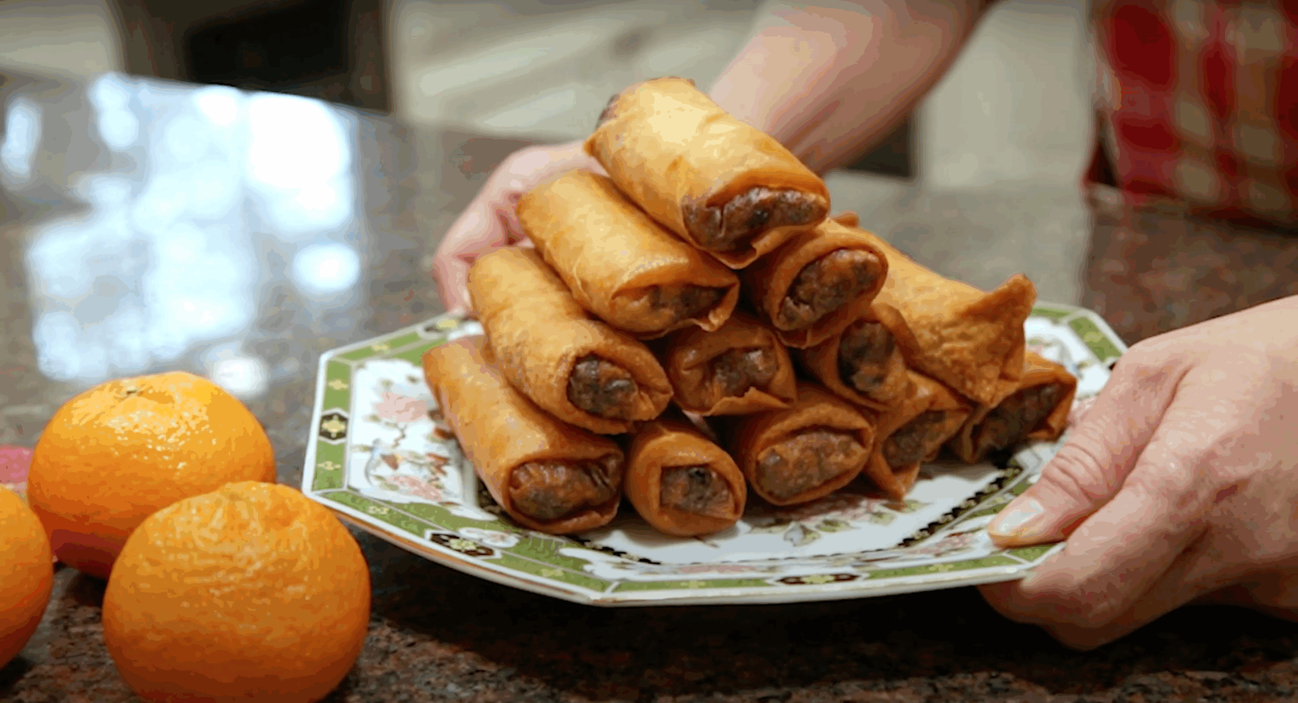 Spring Rolls on a white and green china plate next to oranges.