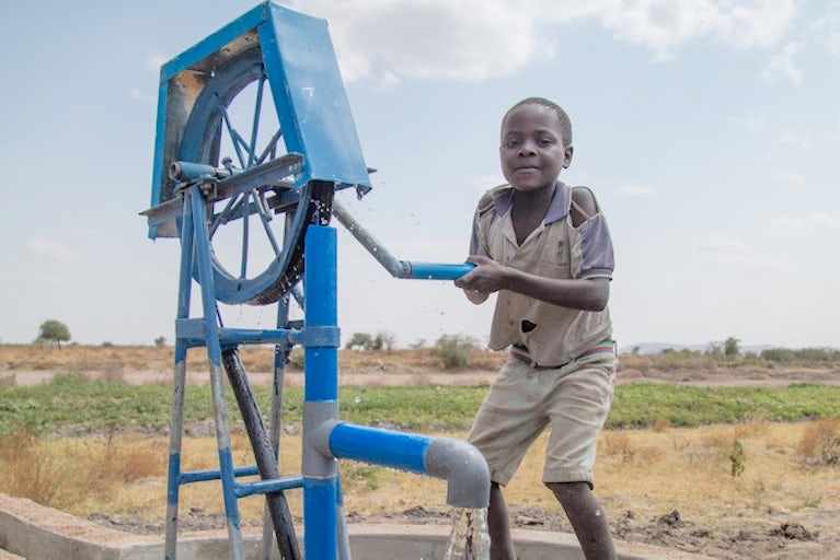 Young boy using a water pump which is pouring into a bucket.