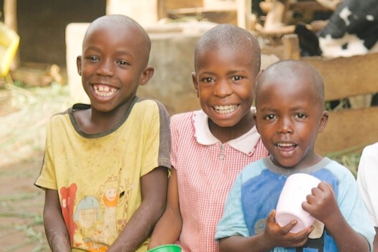 Three children sitting and smiling while holding cups.