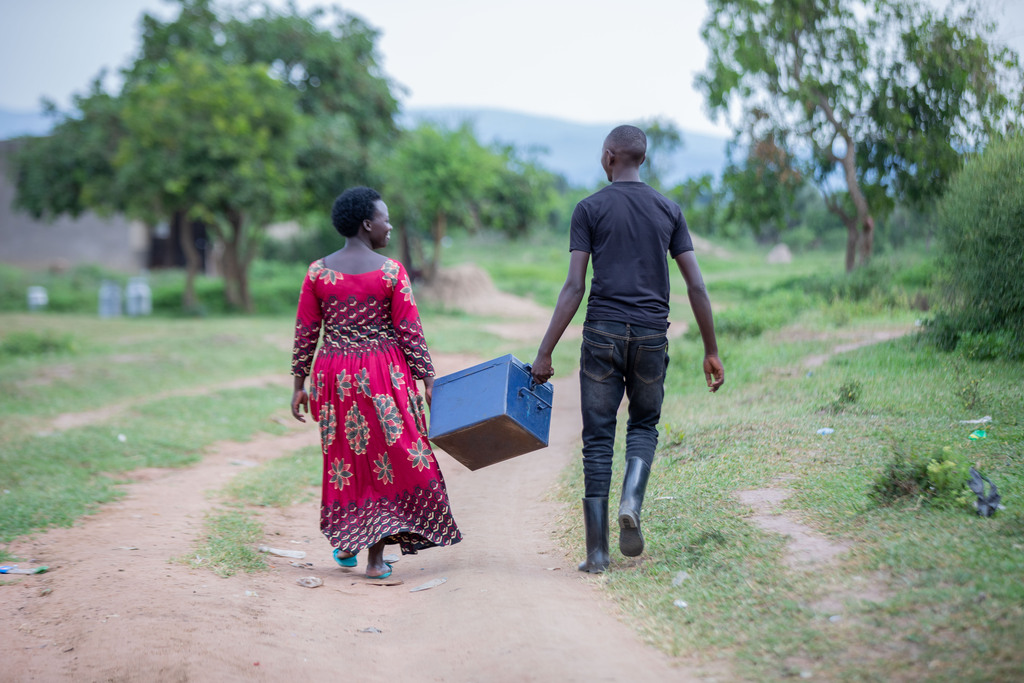 Eric Mugabe and a member of his self-help group, Monica Kabagire, carry a safe containing their savings.