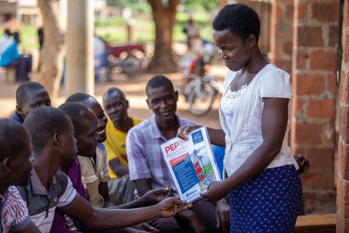 A young woman in Uganda uses a paper flier to teach a small group of youth.