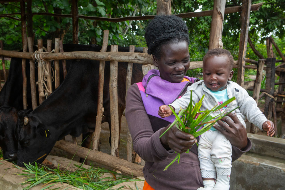 Mother holding her baby and showing them grass clippings while smiling.