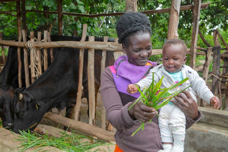 Mother holding her baby and showing them grass clippings while smiling.