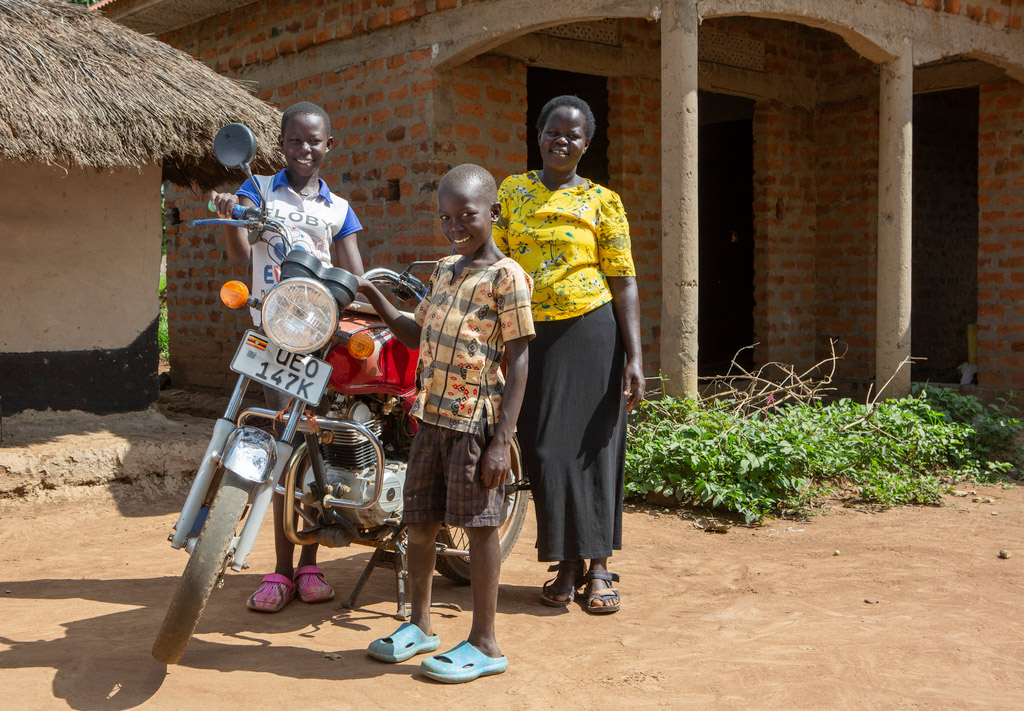 A woman and her two children stand next to a motorcycle outside their home.