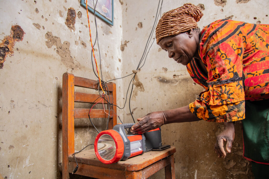 A woman places a solar-powered flashlight on a chair inside her home to charge.