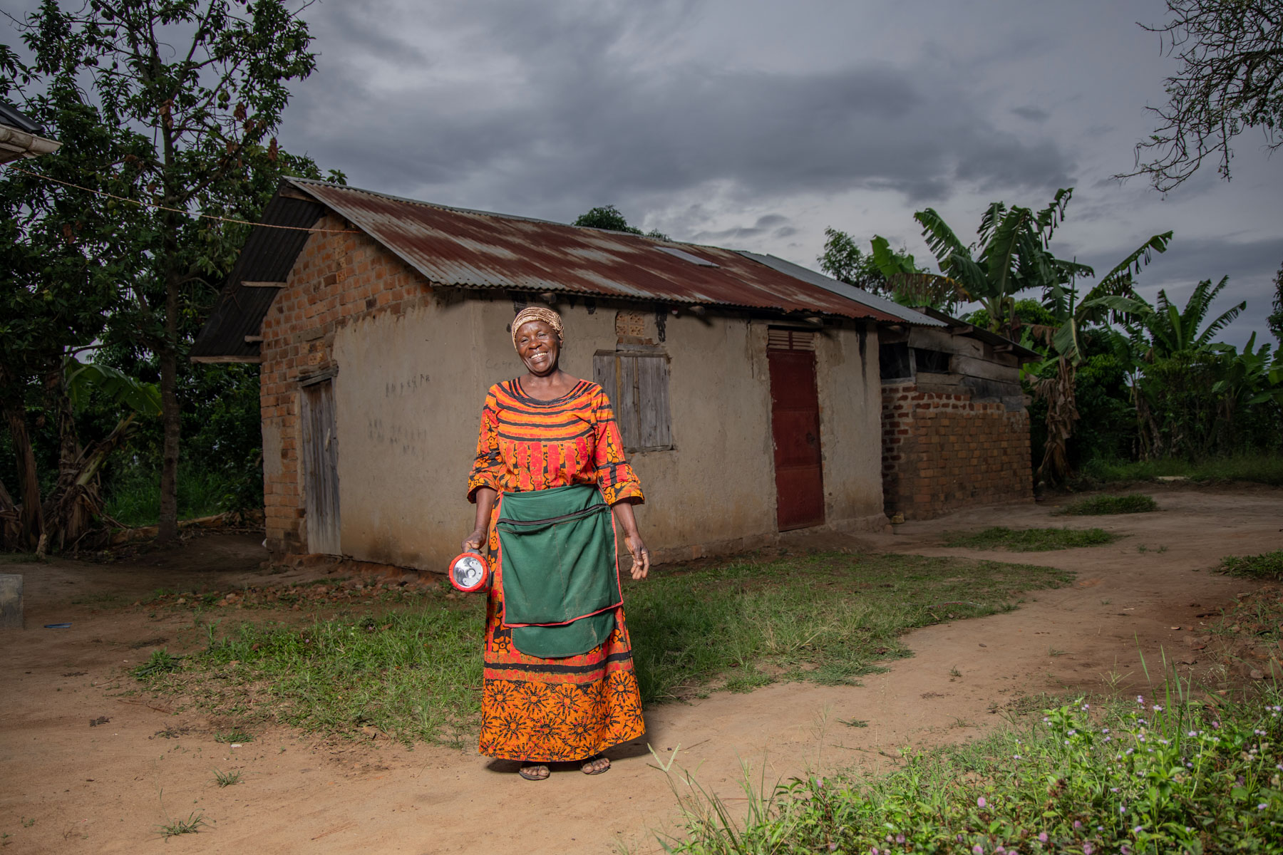 A woman stands outside her home holding a solar-powered flashlight.