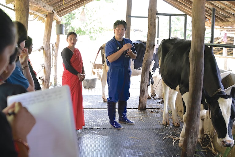 Veteranarian addressing group of people while standing next to a cow.