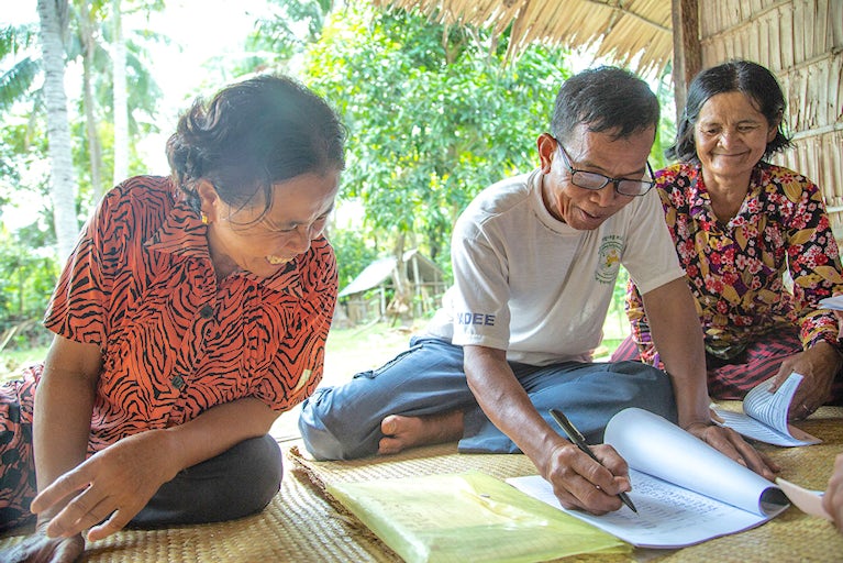 Three Cambodians sitting and working on a ledger.