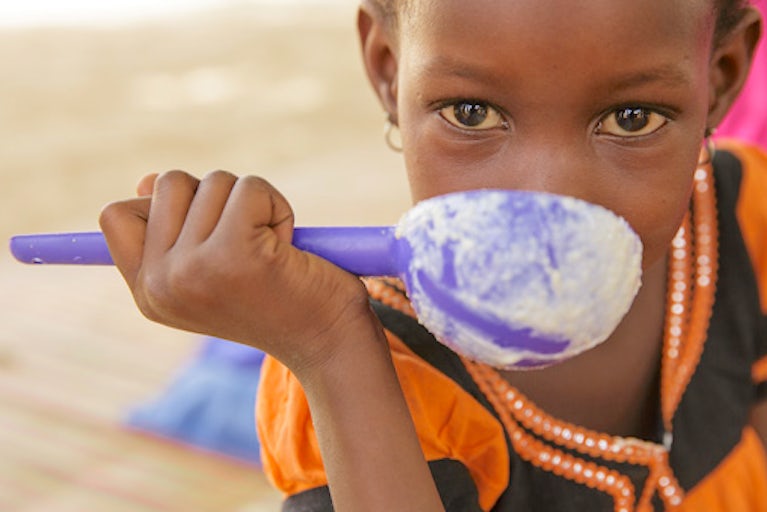 Child looking at the camera while eating from a spoon.
