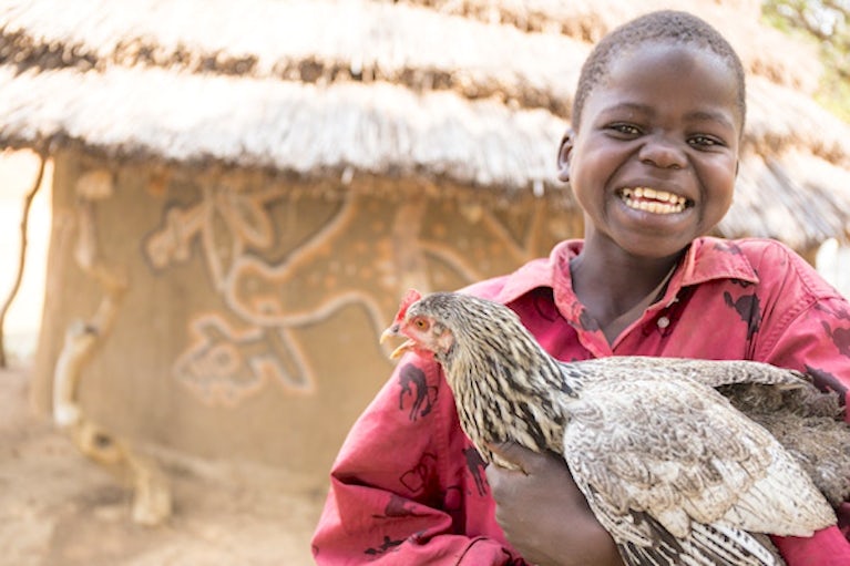 Kid holding a chicken and smiling.