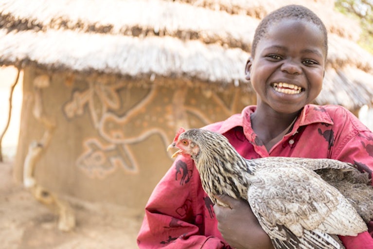 Kid holding a chicken and smiling.