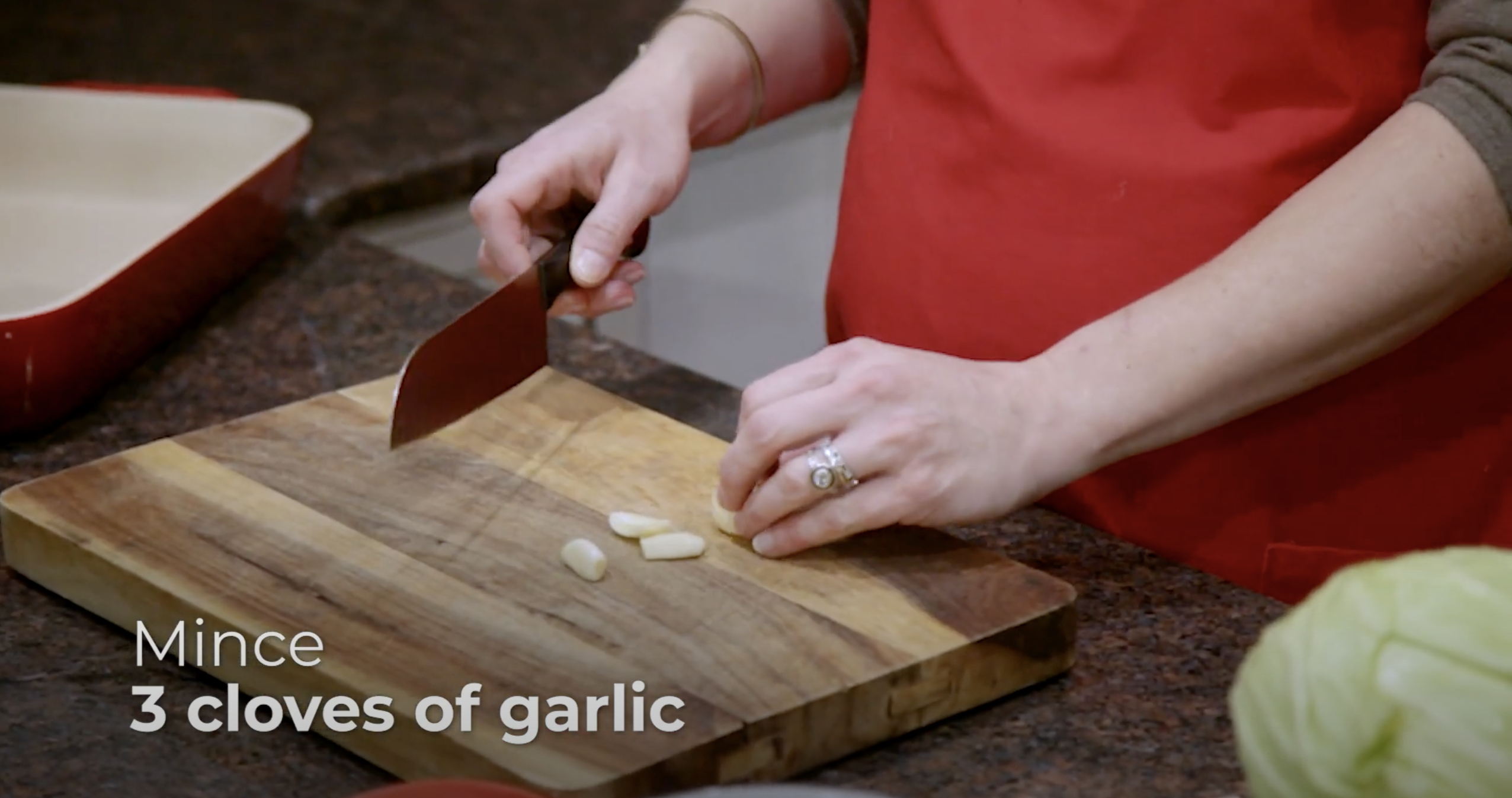 A demonstration shot of mincing garlic - one hand holds a kitchen knife and one holds cloves of garlic.