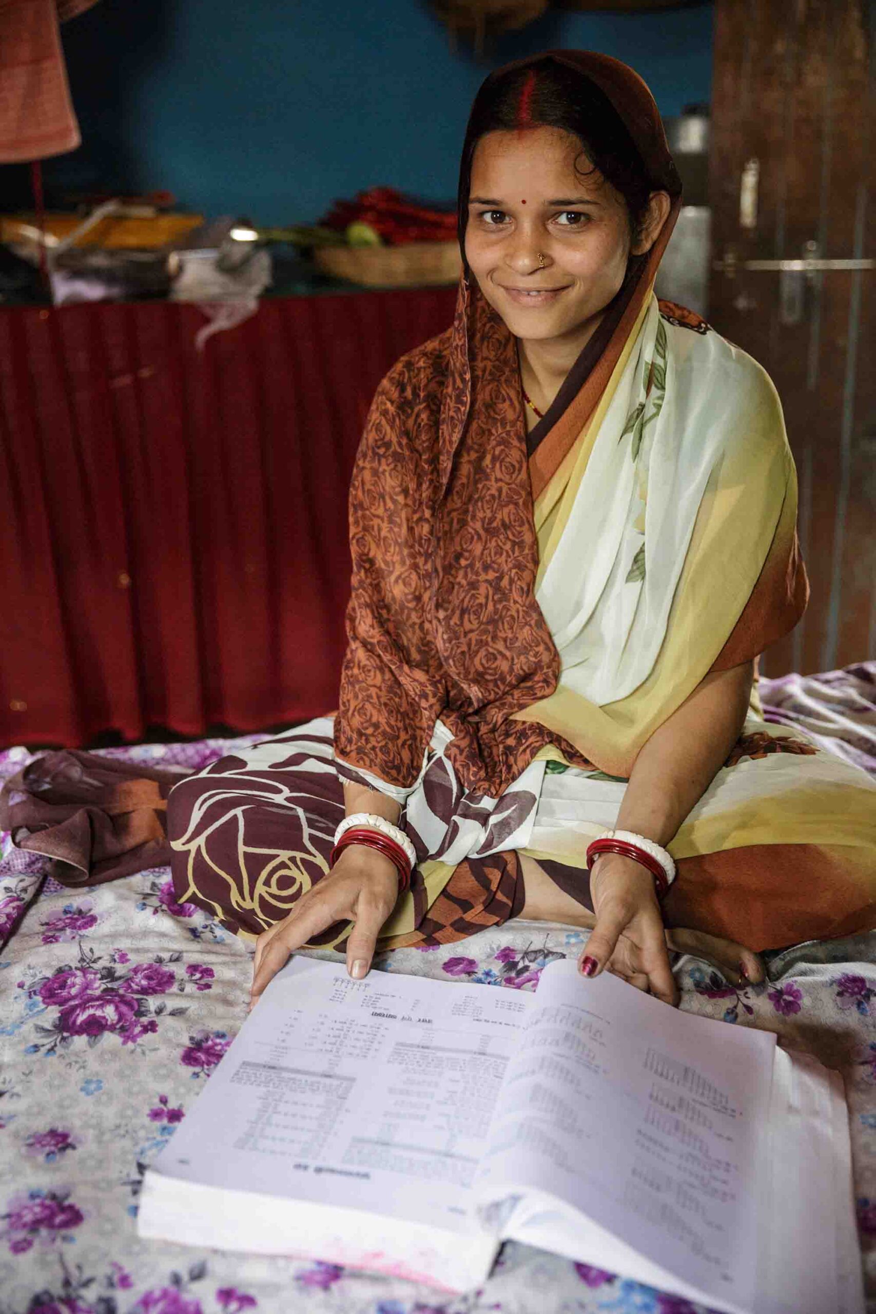 Puja Kumari's bed functioned as her desk, too, as she studied for her college courses. Puja Kumari sits on her bed with one of her textbooks.