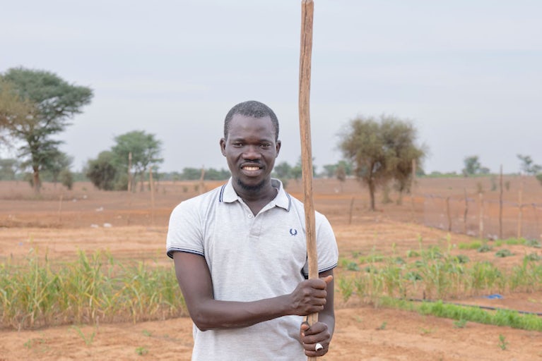 A young man stands holding a wooden stick in a field.