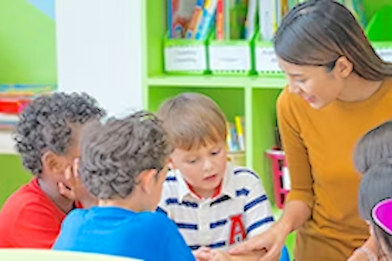 Teacher talking to young students at a table.