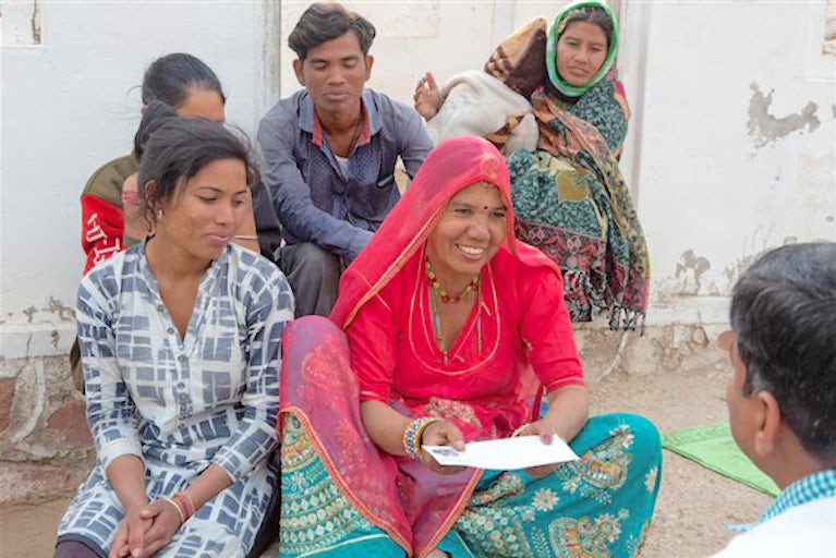 Group of people behind a smiling woman receiving a letter.