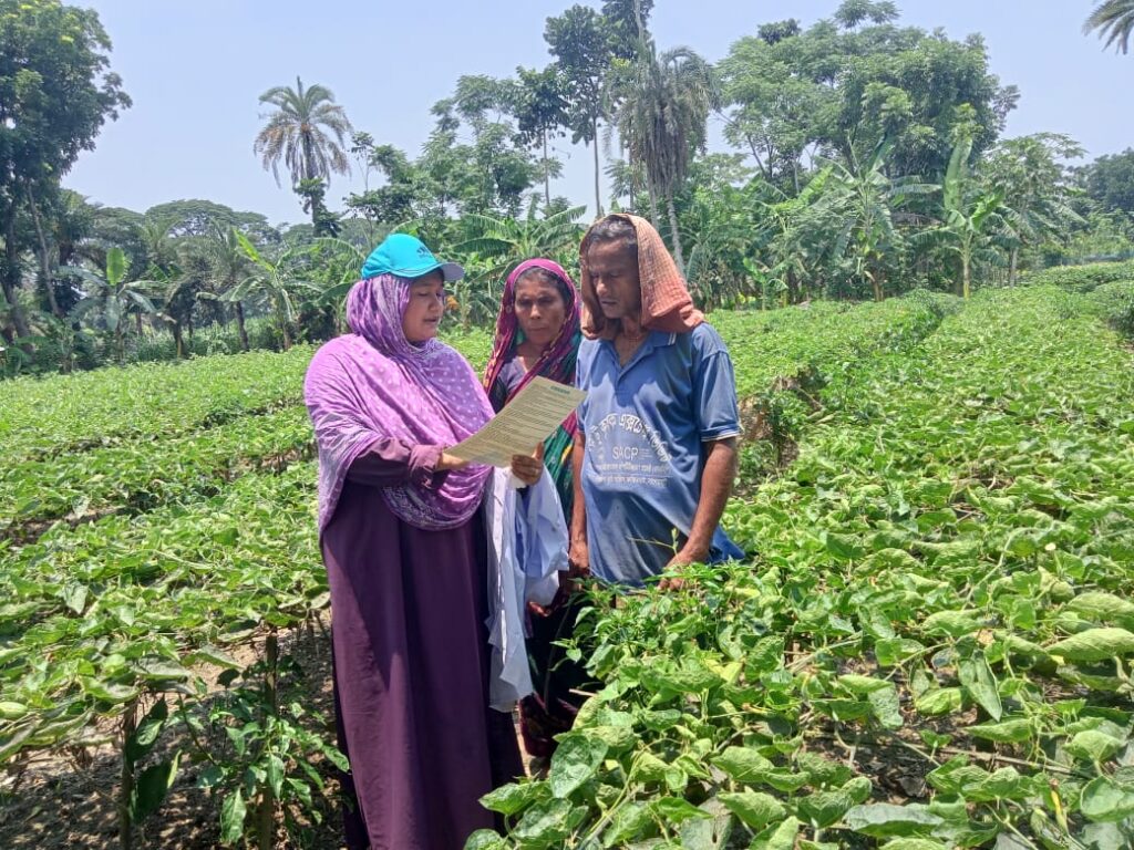 A woman in a purple outfit and blue cap holds a document while standing with two farmers.