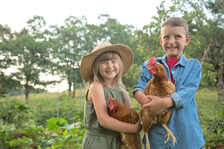 Two small children holding chickens and smiling at the camera.