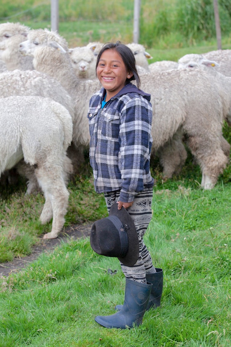 Teen girl standing next to a flock of sheep.