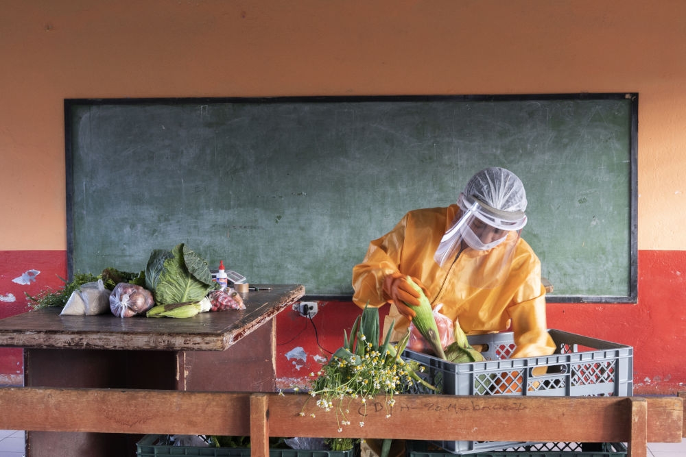 A man wearing a personal protective equipment and face mask is sorting vegetables on a table. 