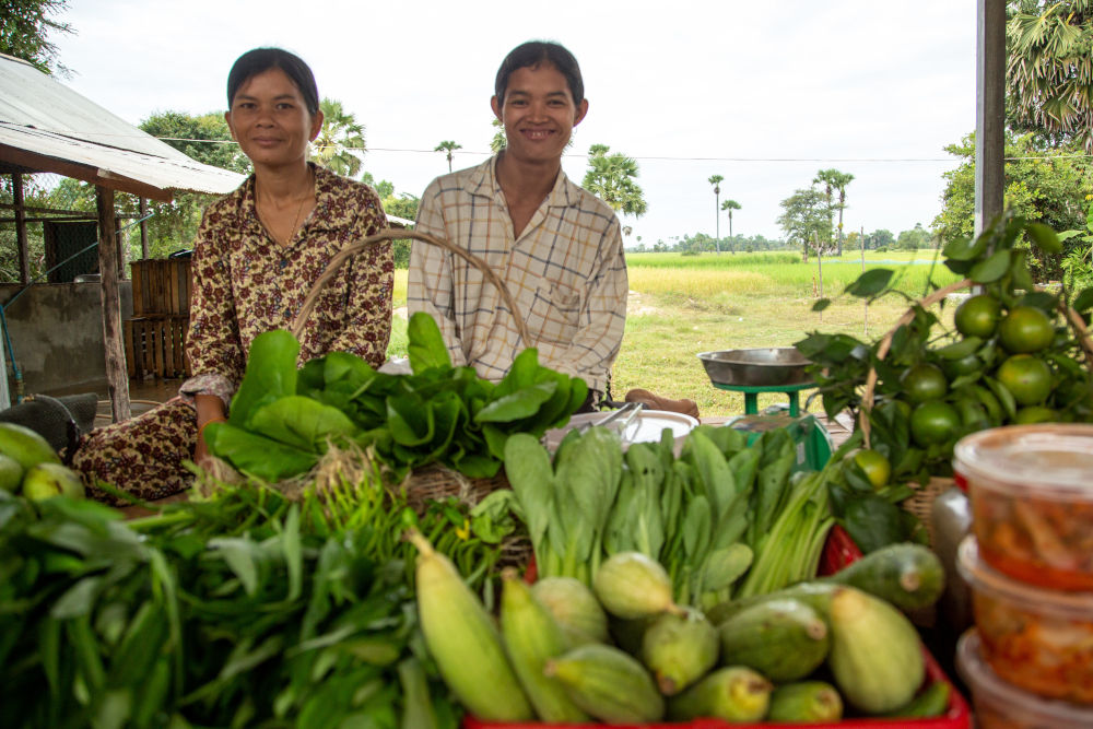 Two women standing behind a bunch of colorful vegetables.