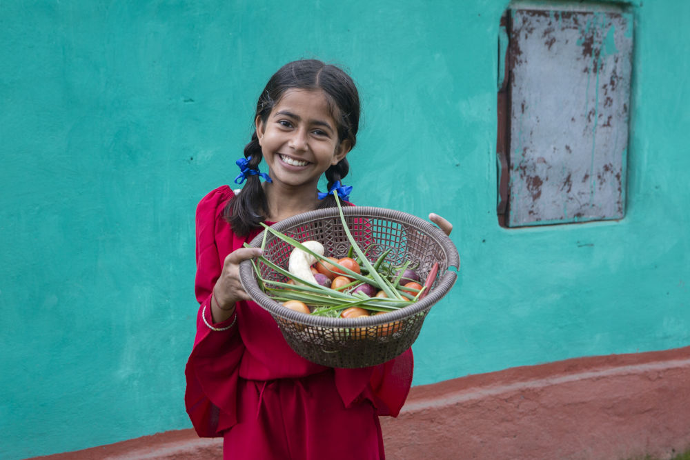 A young girl smiling and holding a basket full of vegetables. 